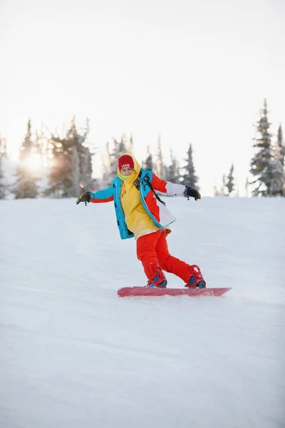 女性は天然のリゾートで雪の山の斜面でスノーボードをしています スキー用具 赤いズボンとニット帽 暖かい黄色のジャケット 選択的焦点 — ストック写真