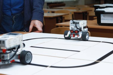 Robots constructors from blocks on wheels. Driving on a black tape. Self-control with path detector. Robotics laboratory at school. Robotics concept. Futuristic scientific concept. Selective focus. clipart