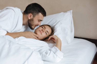 İkisi yatakta. Sakallı bir adam uyuyan bir kadını öper..