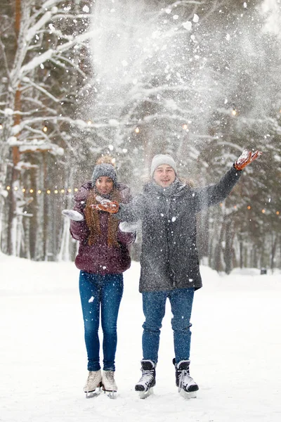 冬服の男と女が公園のスケートリンクで雪を投げます フード ニット帽 雪の森のジャケット 健康的なライフスタイル スポーツの概念 選択的焦点 — ストック写真
