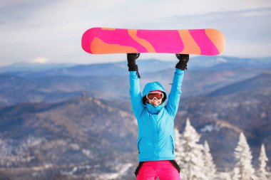 Snowboardcu panoyu yukarıda tutuyor. Kapüşonlu mavi ceket, örgü şapka, kayak gözlüğü. Sağlıklı bir yaşam tarzı. Spor konsepti. Seçici odak.