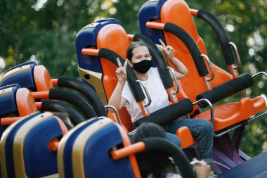 Şehirde yaz eğlence parkında koruyucu maskeli bir kız ya da eğlence parkında. Şehir eğlencesi kavramı, eğlence, eğlence..