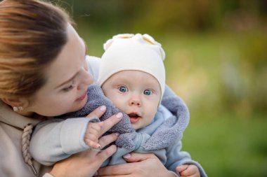 Kadın, mavi gözlü sarışın çocuğu kollarında tutuyor. Mutlu bir çocukluk. Ebeveyn bakımı. Seçici odaklanma. Bulanık arkaplan.