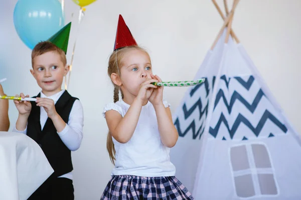 パーティーで楽しんでいるお祝いの帽子の女の子と男の子は 誕生日パイプを吹いてください 幸せな子供時代 子供の幸せ 選択的焦点 — ストック写真