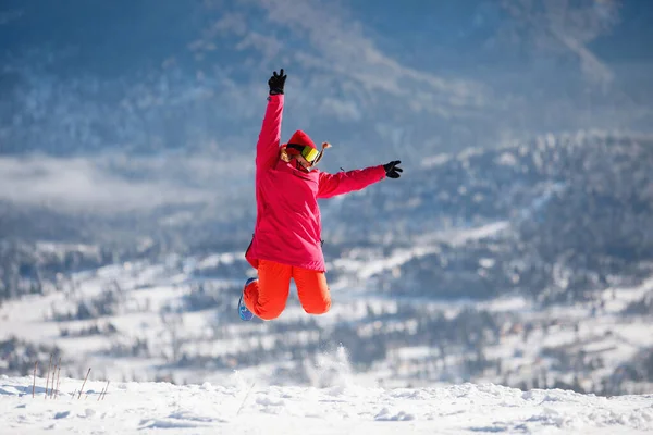 青い山脈の背景にジャンプスキー用具の女性 フード付きジャケット 赤いパンツ スキーゴーグル 健康的なライフスタイル スポーツの概念 選択的焦点 — ストック写真