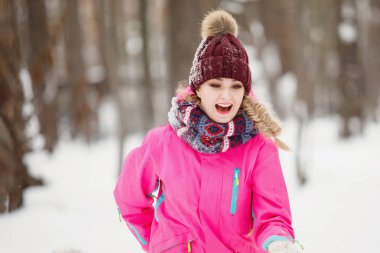 Kış kıyafetleri içinde örgü şapkalı bir kadın ve karlı bir ormanda pembe kapüşonlu bir ceket. Seçici odaklanma. Bulanık arkaplan.