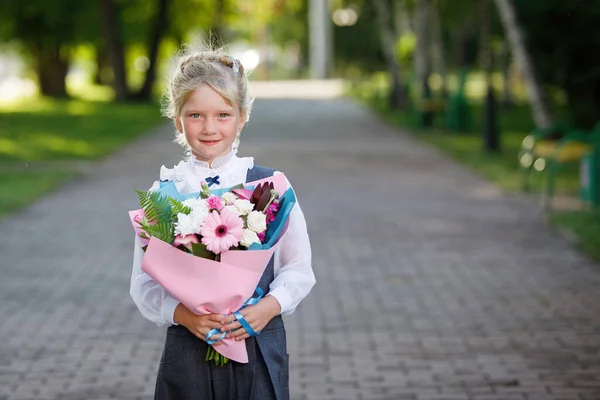 Schoolgirl with a bouquet of flowers at the start of the school year in uniform in a city park. The first time in first class.