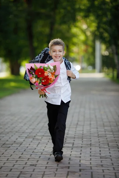 School teenager with a bouquet of flowers at the start of the school year in a white shirt in a city park. The first time in first class.