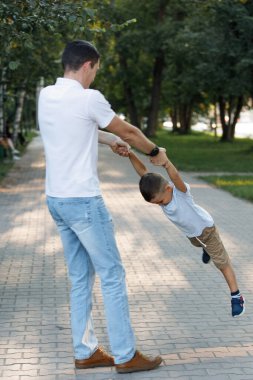 Babası oğlunu bir yaz parkında kollarında döndürüyor. Seçici odaklanma, bulanık arkaplan. Mutlu bir çocukluk. Ebeveyn bakımı.