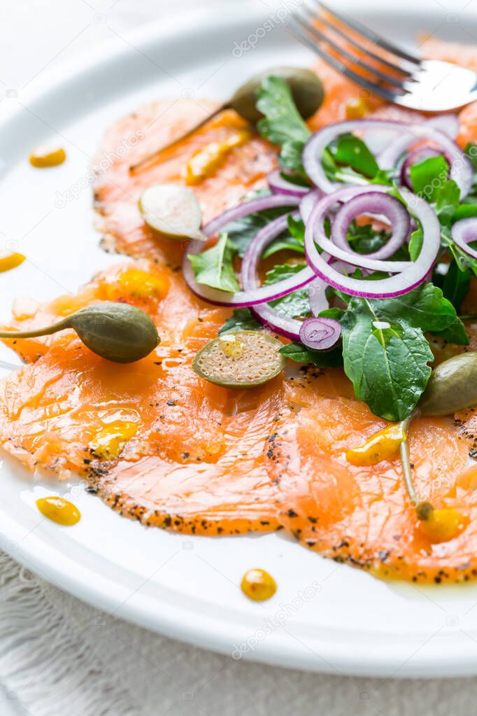 Salmon carpaccio and arugula salad with onions and capers on white plate