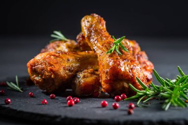 Baharatlı tavuk budu ve siyah arka planda otlar.