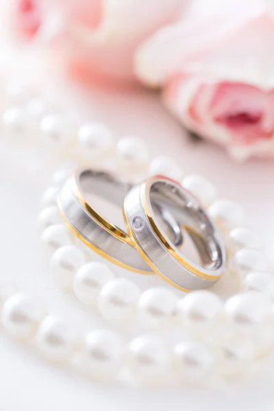 Modern wedding rings with pearl necklace wih pink roses in the background, soft focus