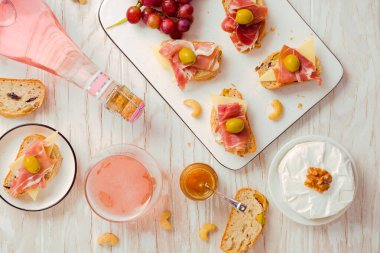 Düz aperatifler ve İtalyan antipastası, camembert, Parma jambonu ve ahşap masada gül şarabı ile açık sandviçler.