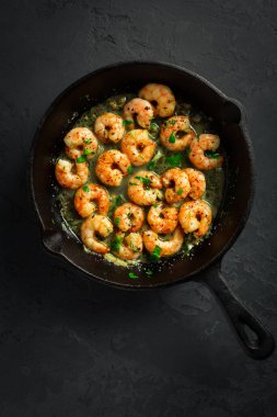 Sarımsaklı karides, zeytinyağı ve siyah arka planda maydanoz.