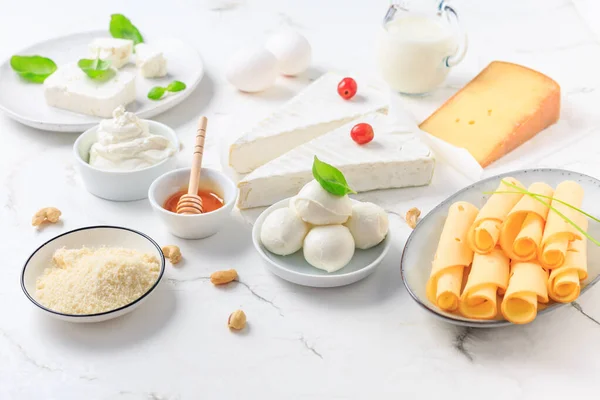 Fresh dairy products on white marble background. Assortment of cheese, honey, milk, yogurt.