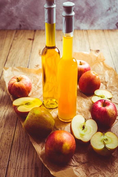 Apple juice with apple vinegar in bottles and fresh apples on wooden background