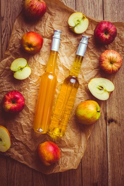 Apple juice with apple vinegar in bottles and fresh apples on wooden background