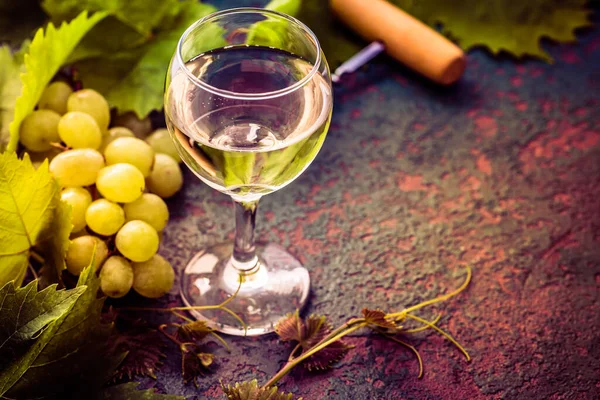 キッチンテーブルの上にボトルオープナーとヴィンテージ設定で白ワインとブドウ — ストック写真