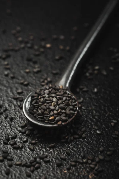 Black sesame seeds in small spoon on black background. Macro studio shot.