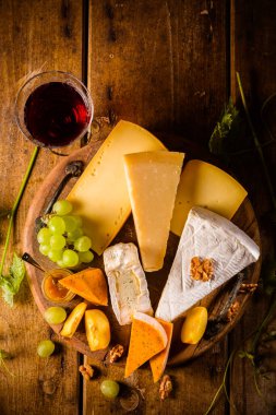 Peynir tabağı, çeşitli peynirler, bir bardak kırmızı şarap, ahşap masada üzümler.
