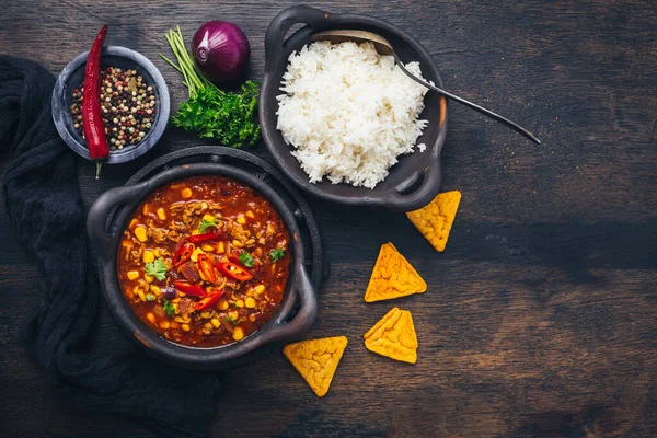 Bowl of chili con carne with rice and toppings on wooden table