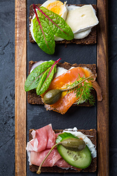 Assortment of open sandwiches on black bread (pumpernickel) on cutting board