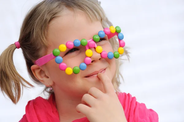 Retrato de niña linda con gafas divertidas, decorado con dulces de colores, smarties, caramelos. Siete años niño divirtiéndose, sonriendo — Foto de Stock