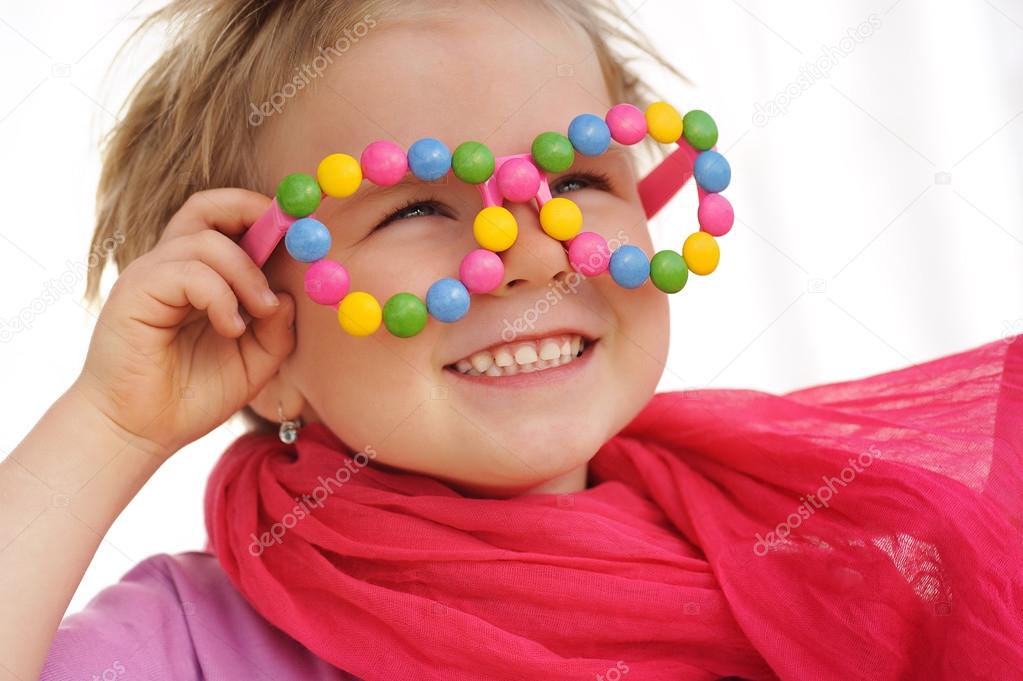 Portrait of cute little girl wearing funny glasses, decorated with colorful sweets, smarties, candies. Four years old child having fun, smiling