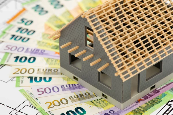 model home standing on construction plan with Euro currency banknotes