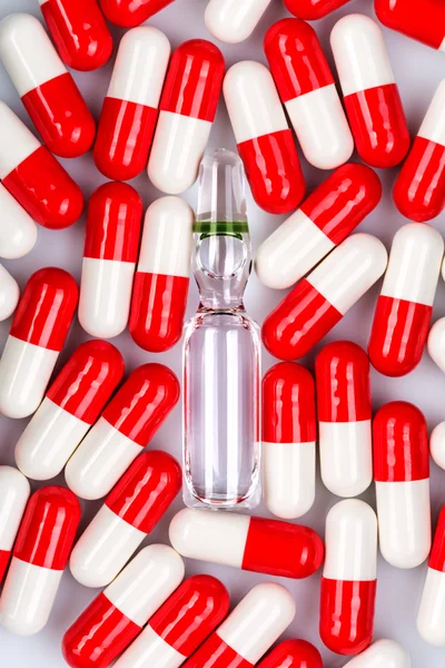 Glass ampoule surrounded by red-white capsules — Stock Photo, Image