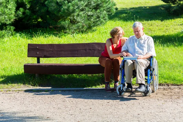 Old man on wheelchair and young woman on a bench — Stock Photo, Image