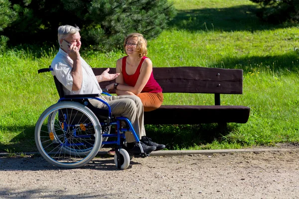 Ηλικιωμένος άντρας στο αναπηρικό καροτσάκι και νεαρή γυναίκα σε ένα παγκάκι — Φωτογραφία Αρχείου