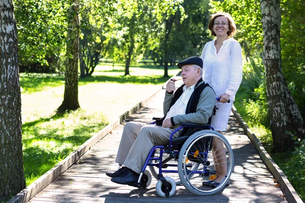 Old man on wheelchair and young woman in the park — Stock Photo, Image