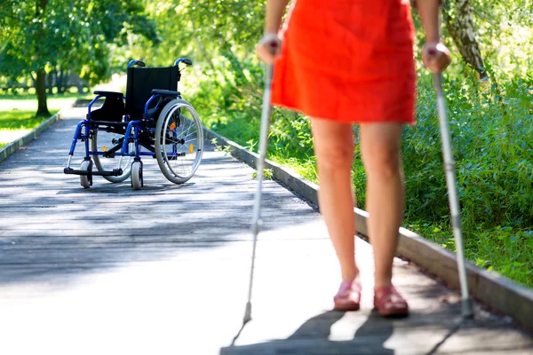 Rullstol och kvinna öva gå på kryckor — Stockfoto