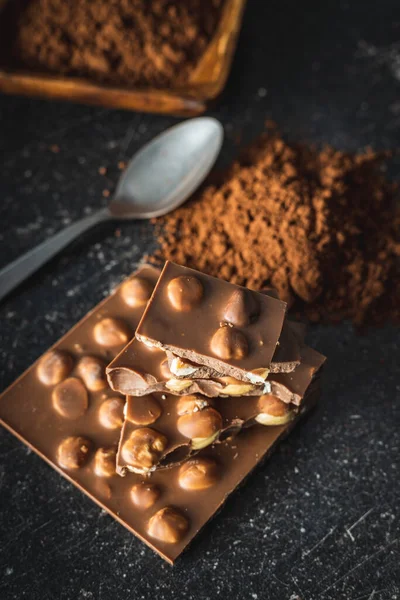 黒テーブルの上にヘーゼルナッツとココアパウダーのナッツチョコレート — ストック写真