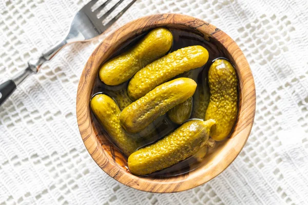 Small pickles. Marinated pickled cucumbers in wooden bowl on white table. Top view.