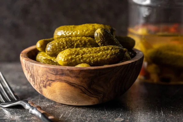 Small pickles. Marinated pickled cucumbers in wooden bowl on black table.