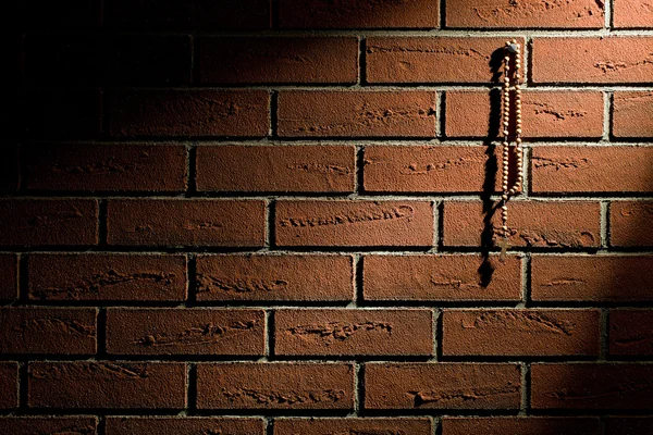 Rosary beads hanging on brick wall — Stock Photo, Image