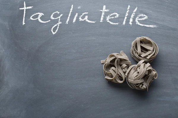 Black tagliatelle pasta on chalkboard — Stock Photo, Image