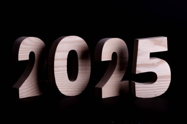 2025 yıllık büyük ahşap sayılar üst üste biniyor. Siyah arkaplanda sert ahşap karakterler