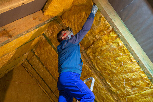 The man insulates the attic of the house with mineral wool