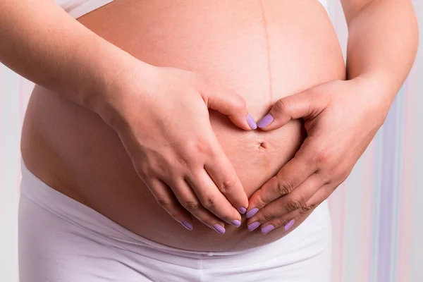 Mulher de mãos dadas na barriga grávida — Fotografia de Stock