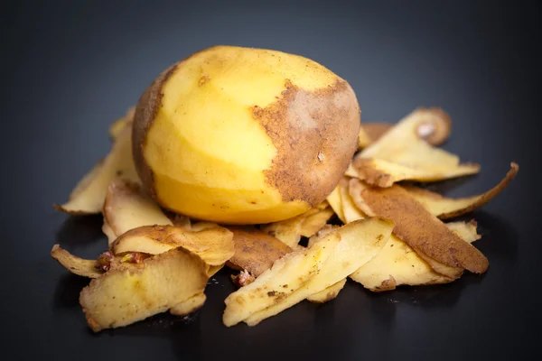 Patate pelate crude e bucce di patate su fondo nero — Foto Stock
