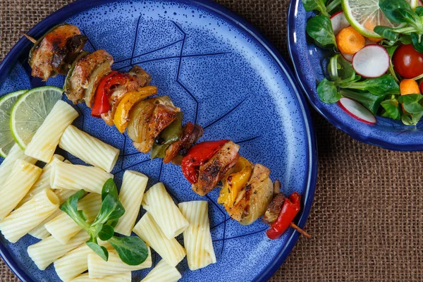 Gegrillte Fleischspieße mit Pasta auf blauem Teller mit Gemüsesalat — Stockfoto