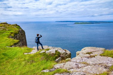 Kuzey İrlanda, İngiltere 'de uçurumun kenarında sırt çantalı bir turist duruyor.