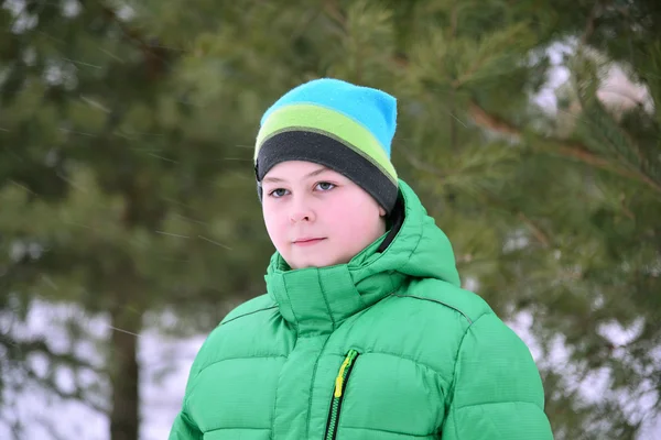 Jongen tiener in groene jas op winter dennenbos — Stockfoto