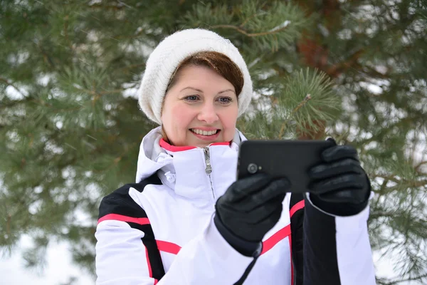 Donna sportiva con smartphone nella foresta invernale di pini — Foto Stock
