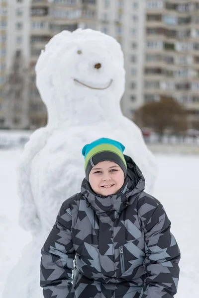 Мальчик-подросток стоит у большого снеговика — стоковое фото