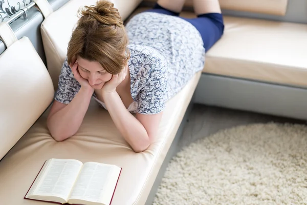 Mujer leyendo un libro tumbado en el sofá —  Fotos de Stock