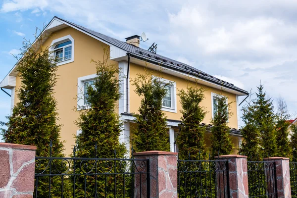 Mooi geel huis met hek en dennenbomen — Stockfoto